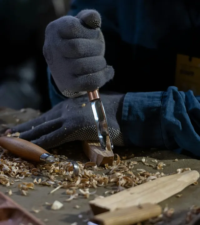 Gloved hands carving wood with a chisel on a workbench